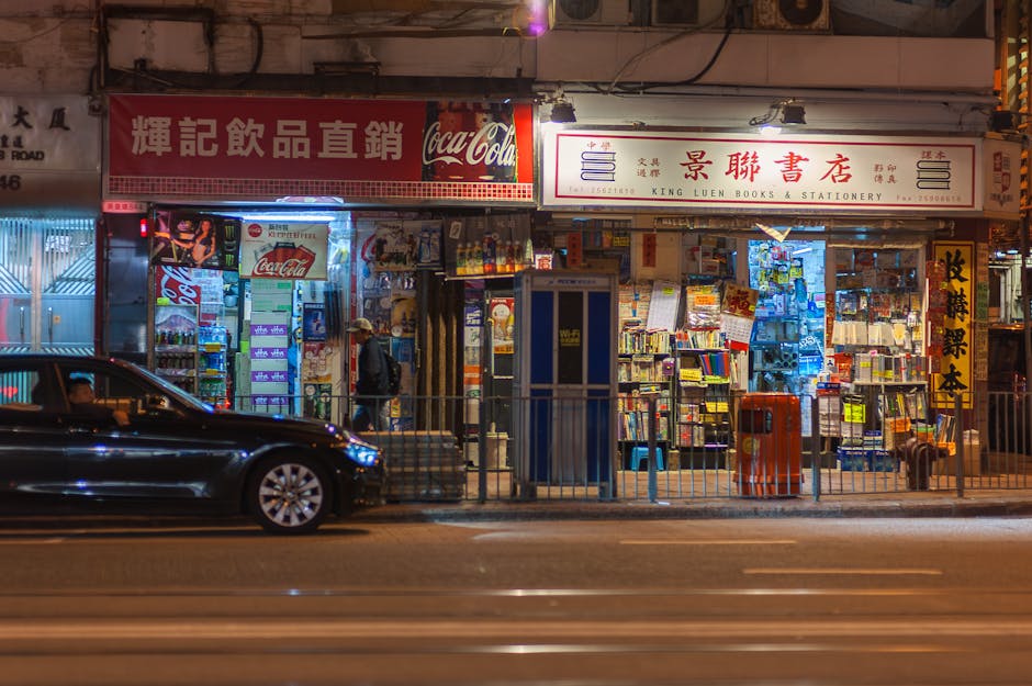 Vibrant Hong Kong street at night with illuminated book and stationery shop, car passing by.